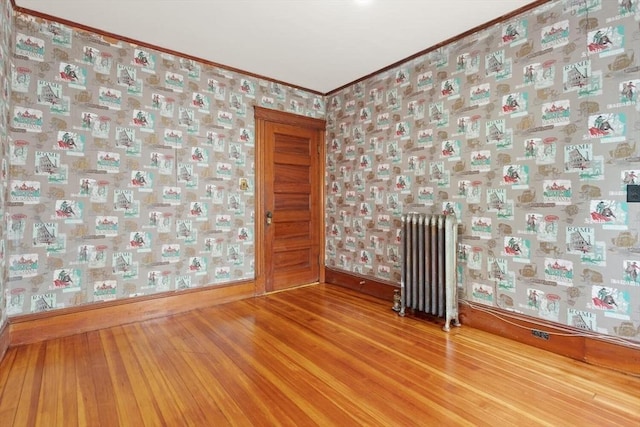 empty room with crown molding, wood finished floors, baseboards, radiator heating unit, and wallpapered walls