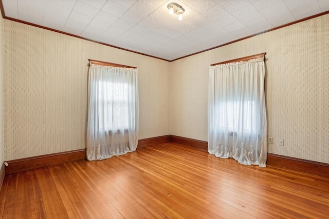 unfurnished room featuring wallpapered walls, ornamental molding, baseboards, and hardwood / wood-style flooring