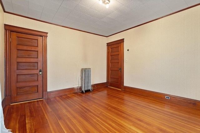 empty room with wood-type flooring, ornamental molding, radiator, and baseboards