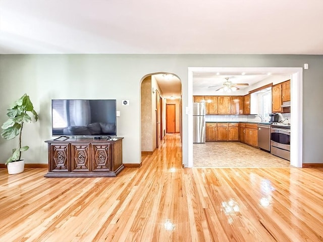 kitchen with brown cabinetry, light wood-style flooring, arched walkways, and stainless steel appliances