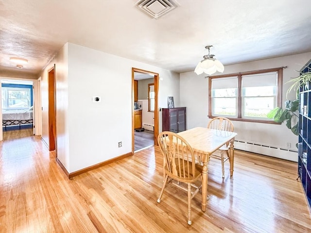 dining space featuring a baseboard heating unit, light wood-style flooring, visible vents, and a wealth of natural light