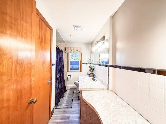 bathroom featuring tile walls, a baseboard heating unit, toilet, wood finished floors, and vanity