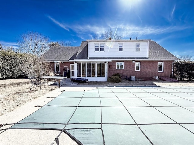 rear view of property featuring brick siding, a covered pool, a patio, and a sunroom