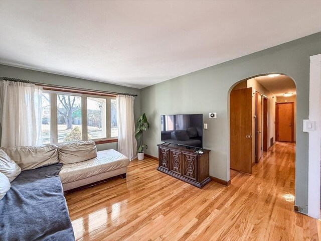 living area with arched walkways, light wood-style flooring, and baseboards