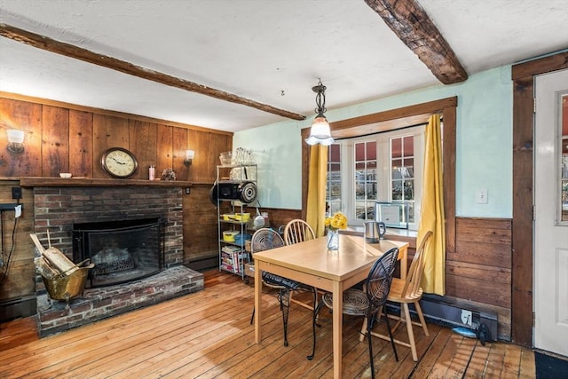 dining room featuring hardwood / wood-style floors, wood walls, beam ceiling, and a brick fireplace