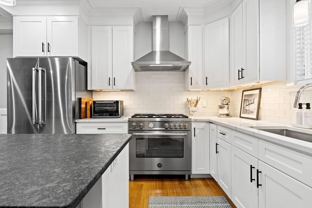 31 Henderson St Unit 1, Arlington, MA 02474 - kitchen featuring stainless steel appliances, wall chimney exhaust hood, a sink, white cabinets, and wood finished floors