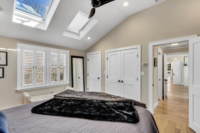 bedroom with lofted ceiling with skylight, recessed lighting, light wood-style flooring, and multiple closets