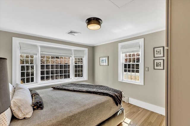 bedroom featuring a baseboard heating unit, visible vents, baseboards, light wood finished floors, and crown molding