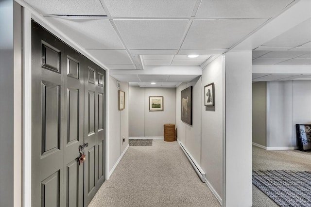 corridor with carpet floors, a paneled ceiling, a baseboard heating unit, and baseboards