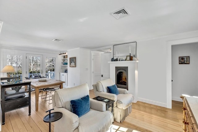 living area with a warm lit fireplace, light wood finished floors, visible vents, and baseboards