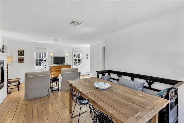 dining area featuring light wood-style flooring, a fireplace, visible vents, and crown molding