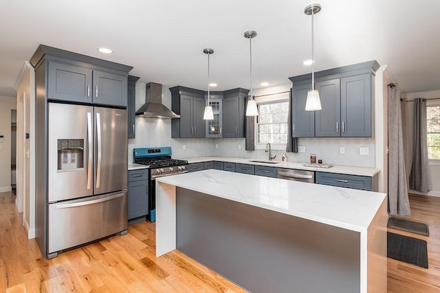 kitchen featuring decorative light fixtures, wall chimney range hood, stainless steel appliances, and a kitchen island