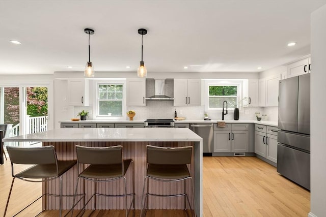 kitchen with stainless steel appliances, wall chimney exhaust hood, backsplash, a center island, and light wood-style flooring