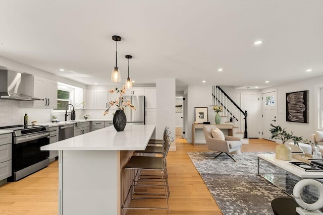 kitchen with stainless steel appliances, wall chimney exhaust hood, recessed lighting, backsplash, and a kitchen island