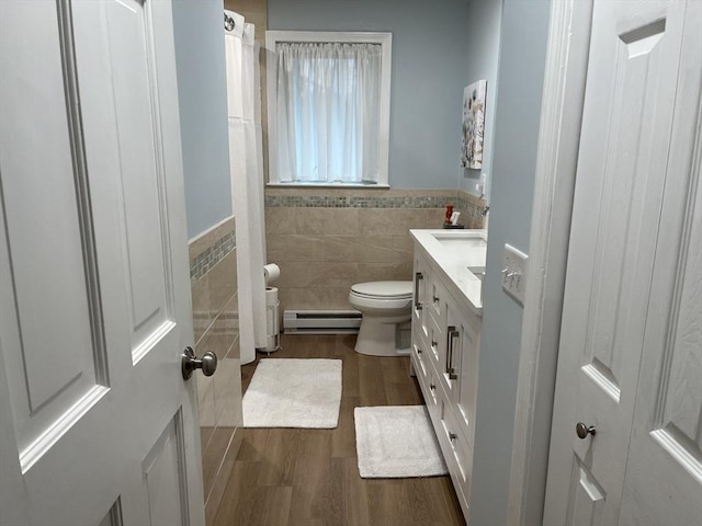 bathroom featuring baseboard heating, wood-type flooring, toilet, vanity, and tile walls