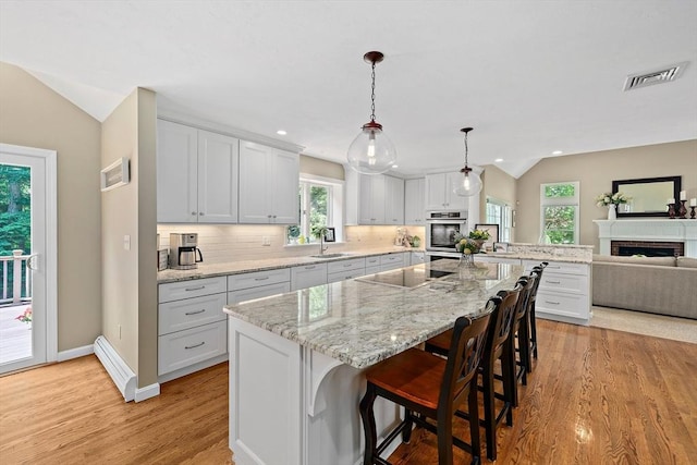 148 Old Schoolhouse Ln, Hanover, MA 02339 - kitchen with vaulted ceiling, stainless steel double oven, light wood finished floors, black electric cooktop, and a breakfast bar area