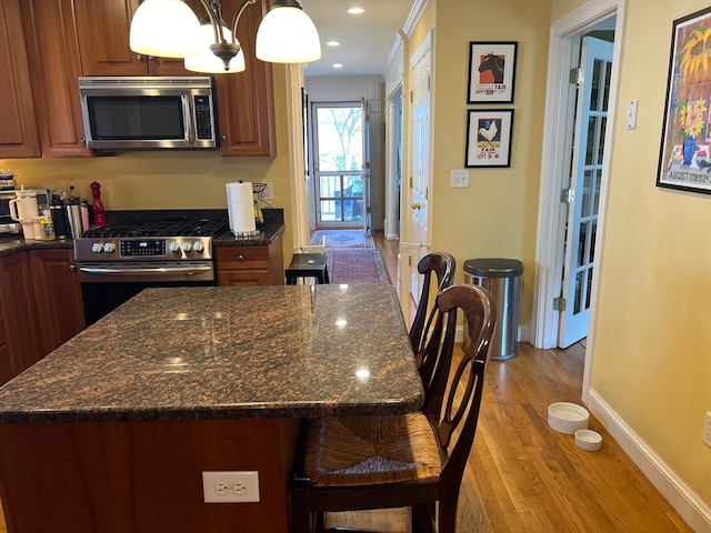 kitchen featuring a notable chandelier, a kitchen island, light hardwood / wood-style flooring, appliances with stainless steel finishes, and dark stone countertops