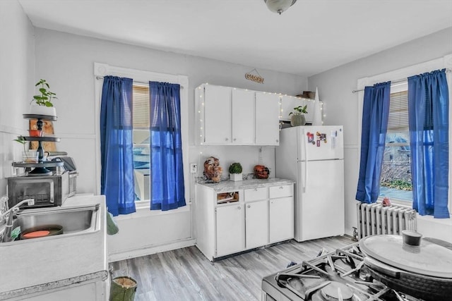 kitchen with radiator, light hardwood / wood-style floors, white cabinets, range, and white fridge