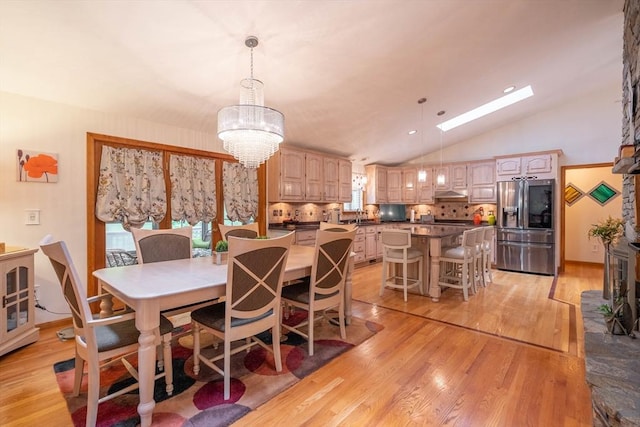 dining room featuring a chandelier, vaulted ceiling, light wood finished floors, and a skylight