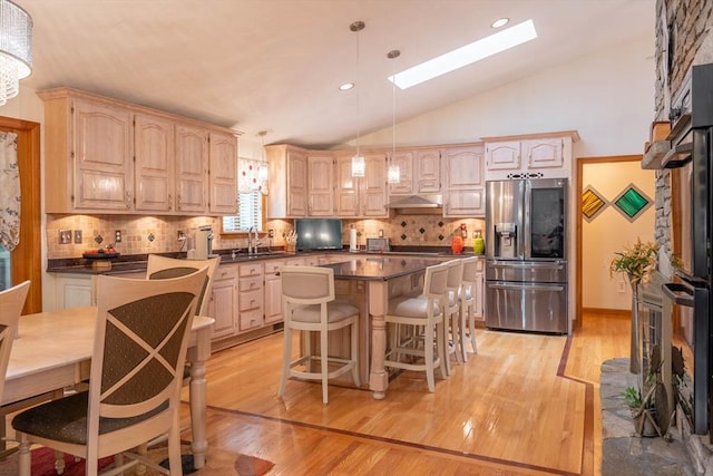kitchen with stainless steel fridge with ice dispenser, a skylight, dark countertops, light brown cabinetry, and vaulted ceiling