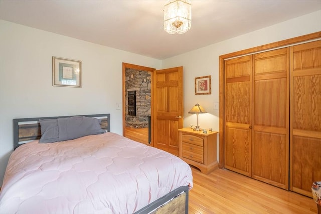 bedroom featuring light wood-style flooring, a closet, and a stone fireplace