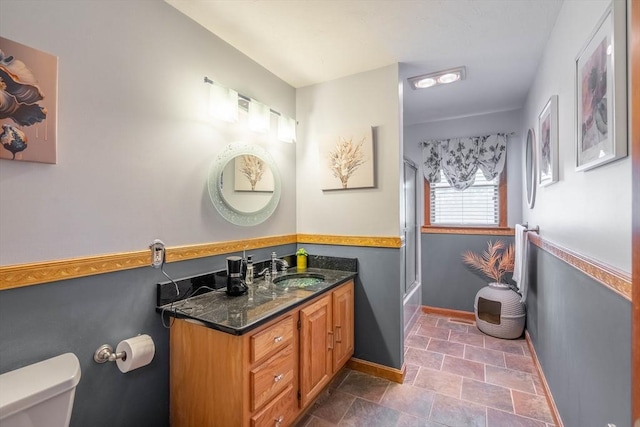 bathroom featuring toilet, baseboards, vanity, stone finish flooring, and bath / shower combo with glass door