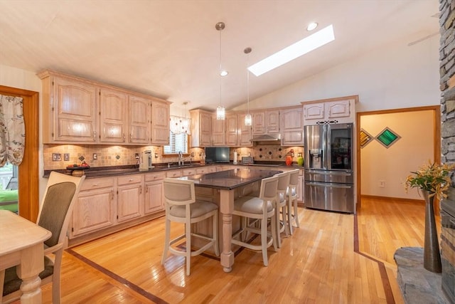 kitchen with stainless steel fridge with ice dispenser, a skylight, a sink, dark countertops, and tasteful backsplash