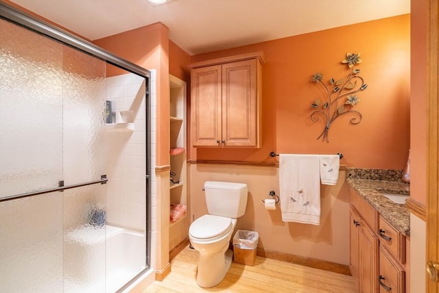 full bath featuring a shower stall, toilet, wood finished floors, vanity, and baseboards