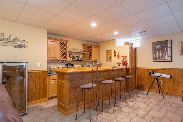 indoor bar featuring wine cooler, a wainscoted wall, a drop ceiling, wood walls, and recessed lighting