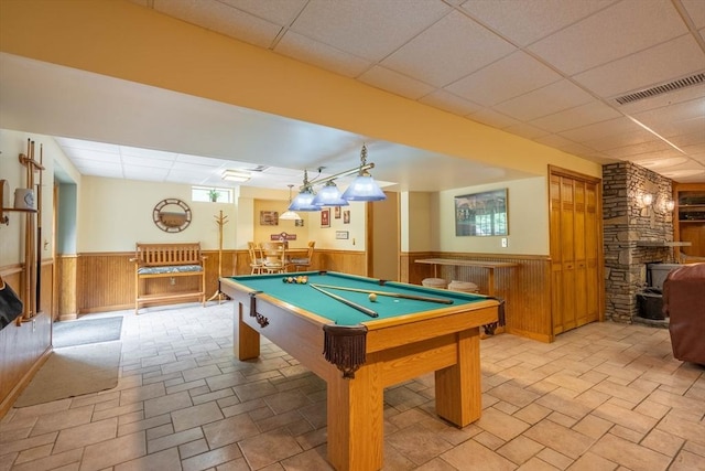 recreation room featuring wainscoting, a drop ceiling, a wood stove, billiards table, and a bar