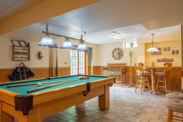 recreation room featuring a wainscoted wall, wooden walls, billiards table, bar area, and a drop ceiling