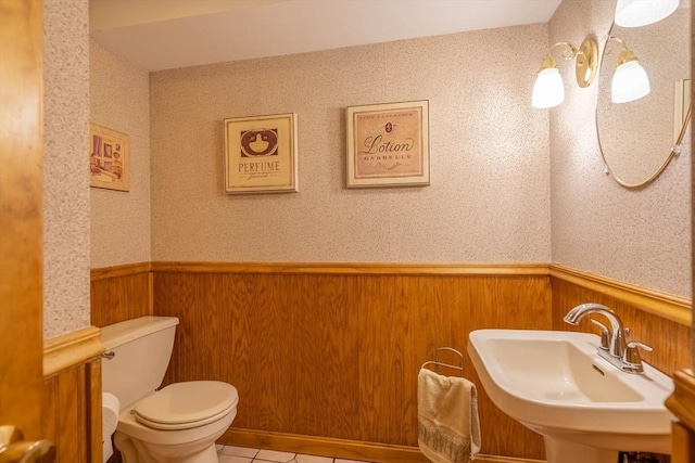 bathroom featuring a wainscoted wall, a sink, toilet, tile patterned flooring, and wooden walls