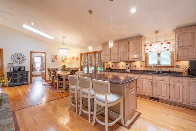 kitchen with a sink, lofted ceiling, light wood finished floors, decorative backsplash, and dark countertops