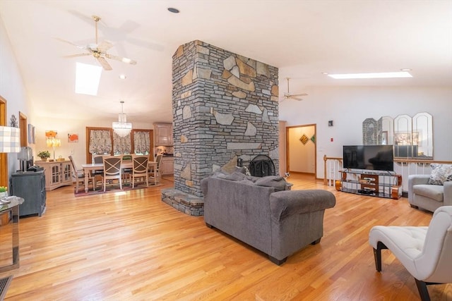 living room with ceiling fan, light wood-type flooring, high vaulted ceiling, a stone fireplace, and a skylight