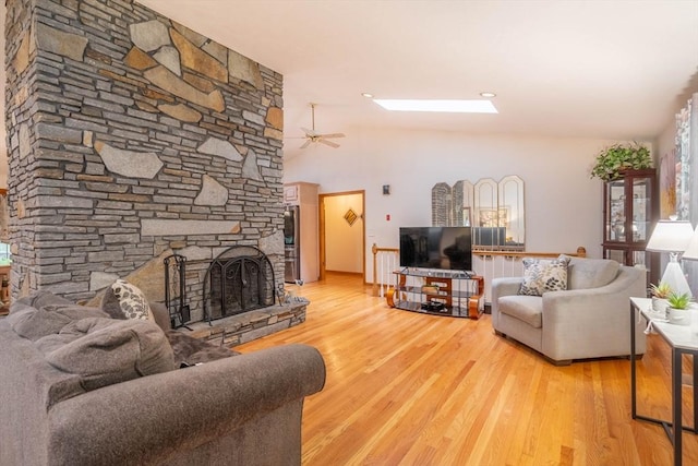 living area with wood finished floors, a stone fireplace, ceiling fan, and a skylight