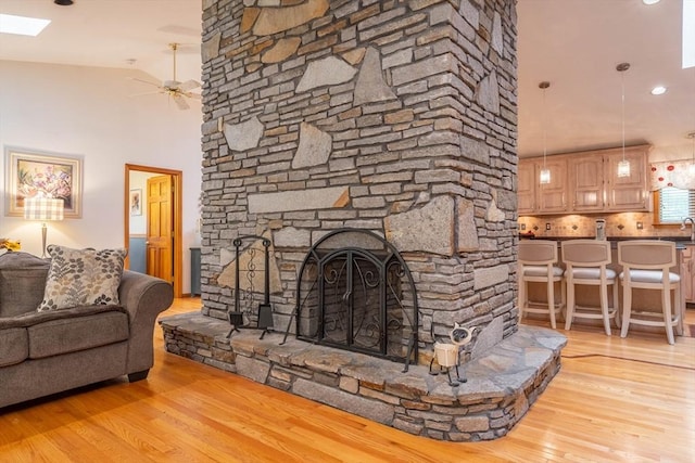living room featuring a ceiling fan, wood finished floors, a stone fireplace, and a towering ceiling