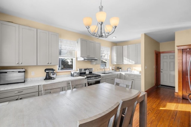 kitchen with light countertops, a sink, wood finished floors, stainless steel gas range, and under cabinet range hood