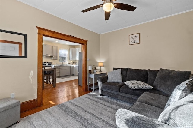 living room with a ceiling fan, crown molding, baseboards, and wood finished floors