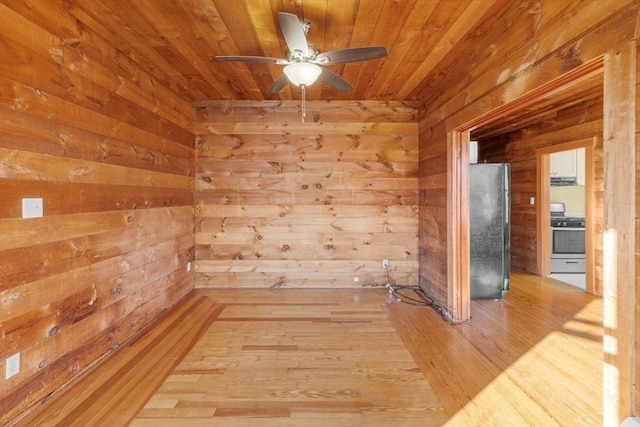 spare room with wooden ceiling, wood walls, light wood finished floors, and a ceiling fan