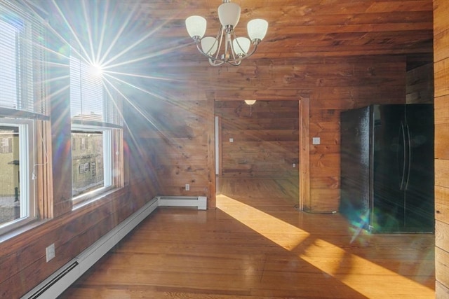 interior space featuring an inviting chandelier, wooden walls, a baseboard heating unit, and wood finished floors