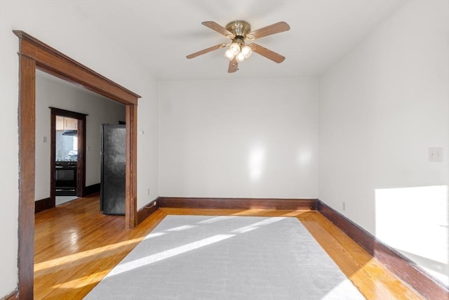 empty room with baseboards, ceiling fan, and light wood-style floors