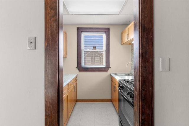 kitchen featuring light tile patterned floors, a sink, baseboards, light countertops, and gas stove