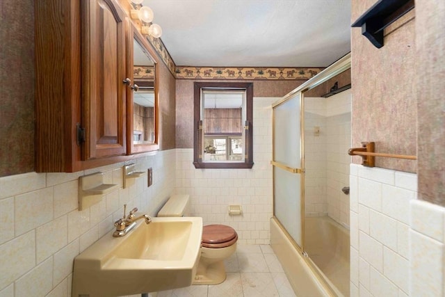 bathroom featuring tile patterned flooring, toilet, combined bath / shower with glass door, tile walls, and a sink