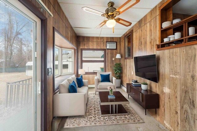 living room with wooden walls, a baseboard radiator, ceiling fan, a wall mounted air conditioner, and light carpet