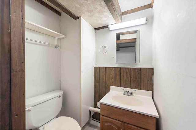 half bath with a wainscoted wall, toilet, wood walls, and vanity