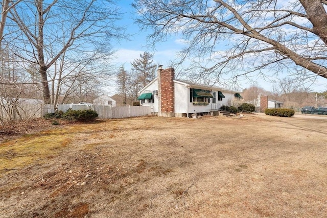 view of side of home with a chimney, a yard, and fence