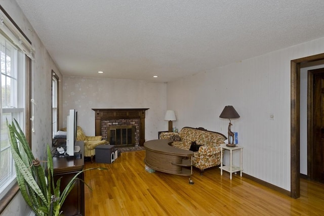 living area featuring a brick fireplace, a textured ceiling, baseboards, and wood finished floors