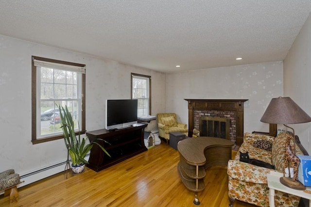 living area featuring a baseboard heating unit, a textured ceiling, wood finished floors, and a fireplace