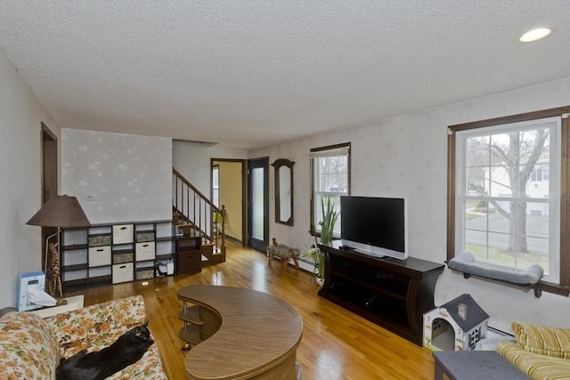 living room featuring a baseboard heating unit, a textured ceiling, wood finished floors, and stairway
