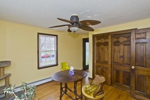 dining room featuring a textured ceiling, ceiling fan, baseboard heating, and light wood-style flooring
